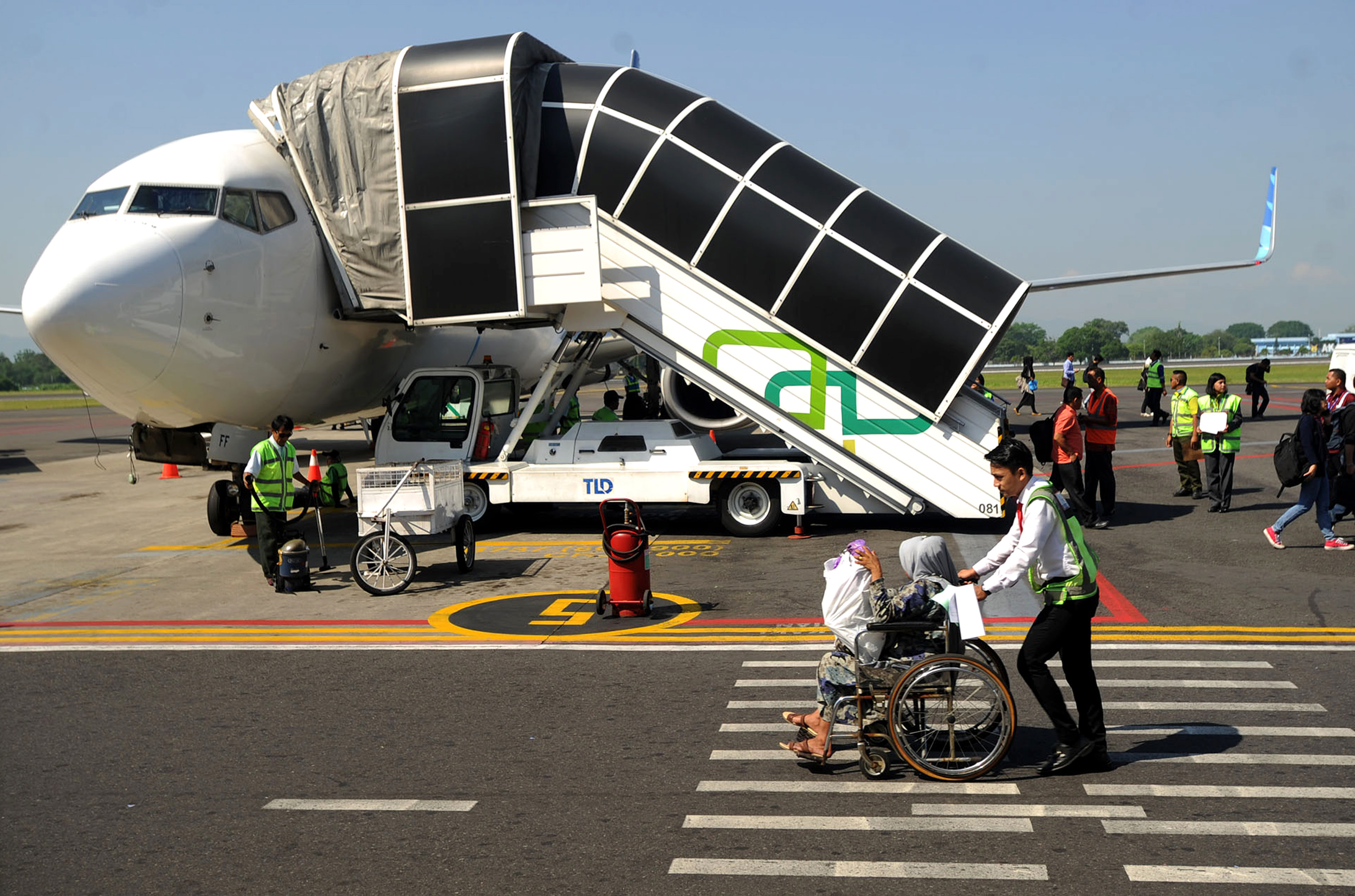 Airport staff helping elderly and sick passengers in wheelchairs to board a plane